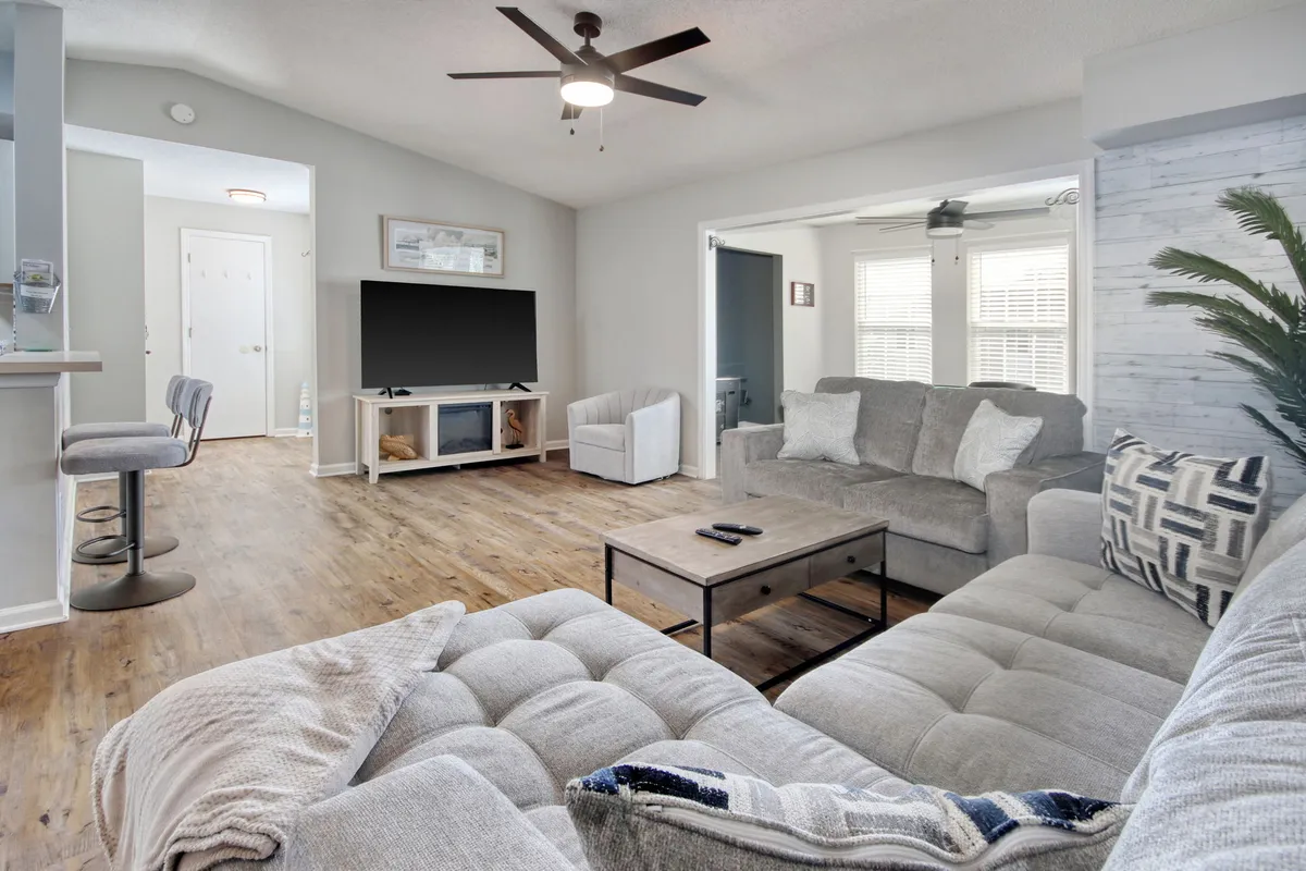 The hero image shows a bright, inviting living room with a comfortable sofa, stylish coffee table, large television, sleek wood flooring, and a modern light fixture. The space is designed for relaxation, entertainment, and quality time with family or friends.