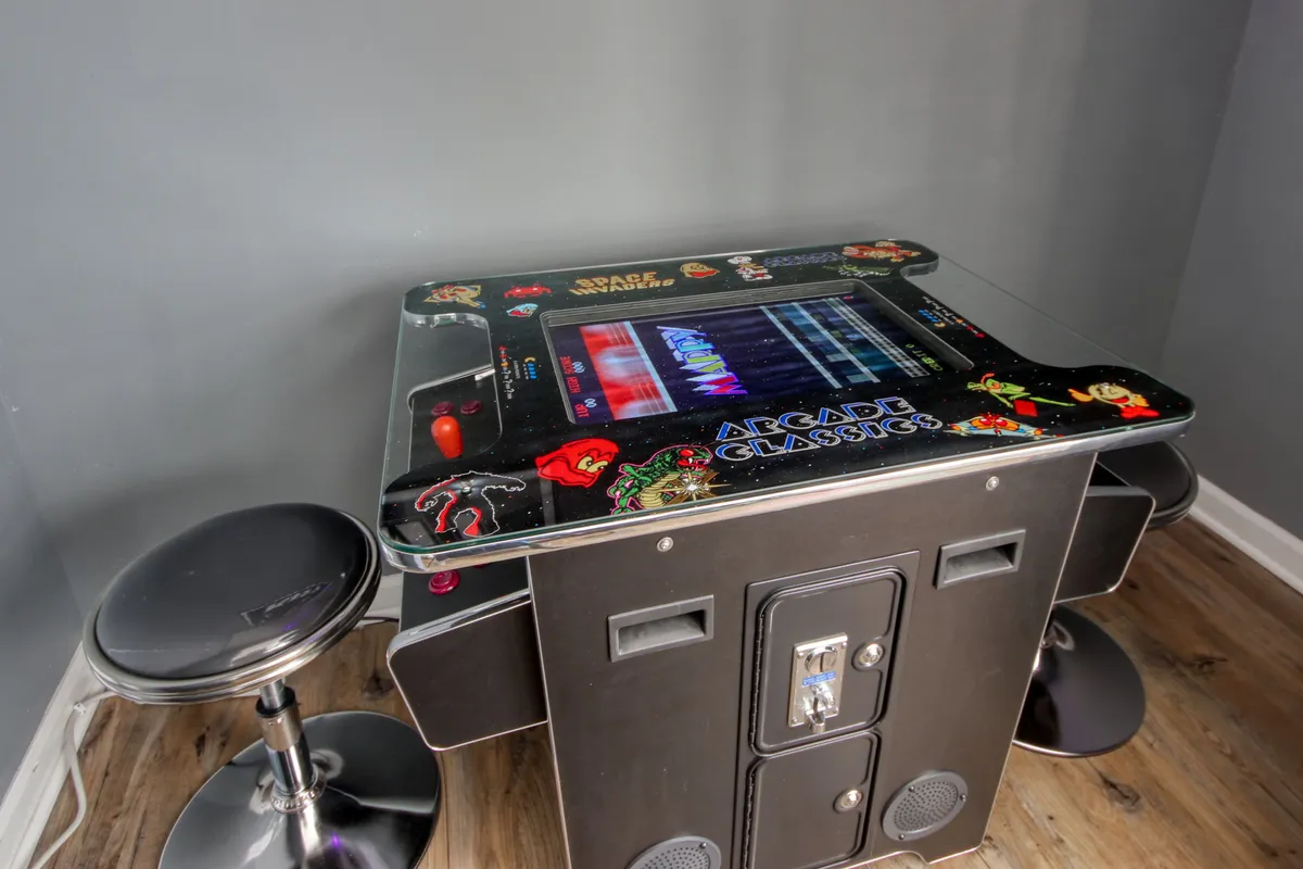 This image showcases an inviting arcade game table surrounded by bar stools, suggesting a lively space for casual entertainment or socializing after a day out. The lighting and setup evoke a feeling of fun and connection, perfect for winding down inexpensively.