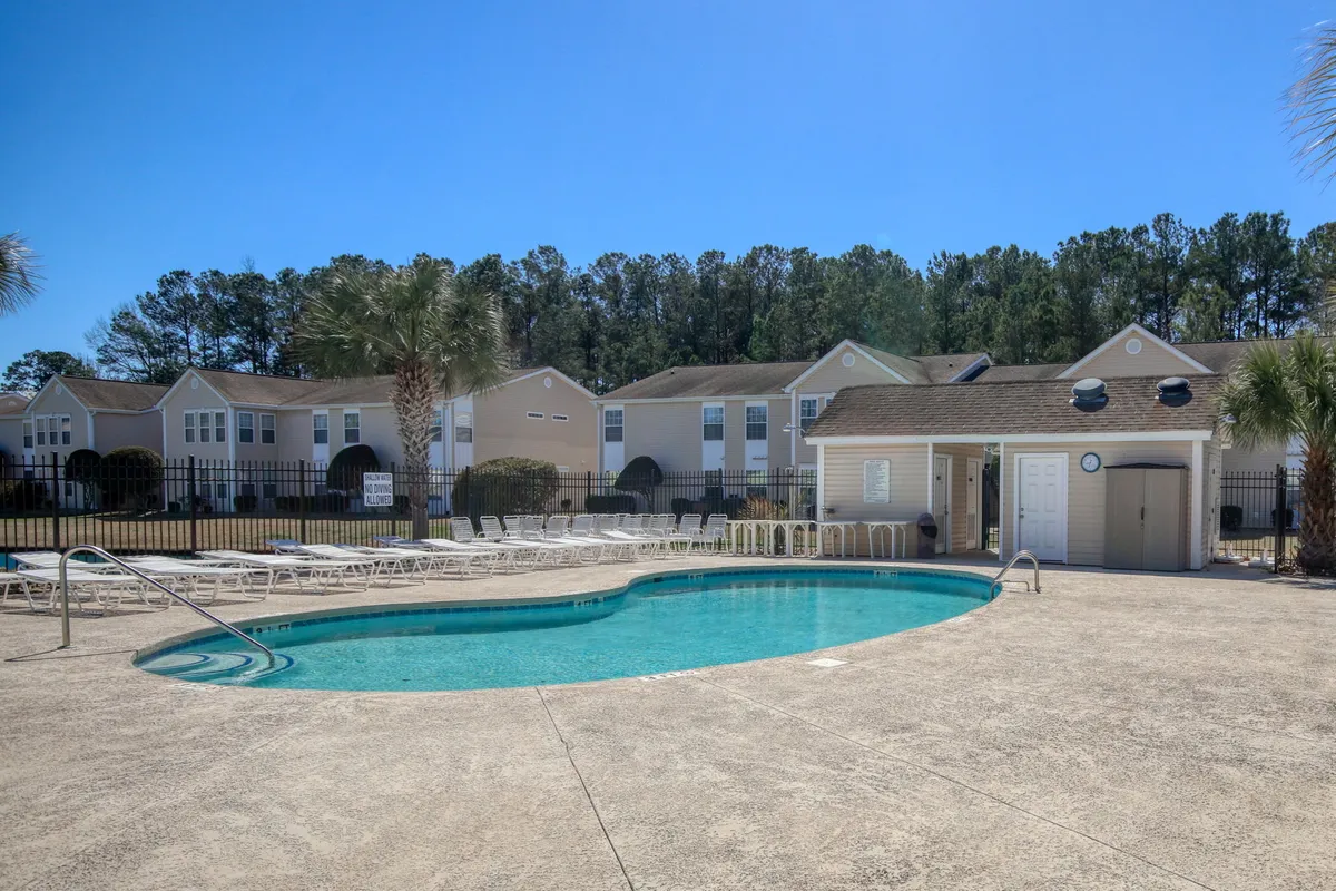 A sun-drenched swimming pool framed by lounge chairs and lush greenery, with residential buildings in the background. The tranquil setting radiates a resort-style ambiance, inviting guests to swim, sunbathe, or relax by the water. The scene also captures hints of vibrant community life, perfect for both quiet mornings and lively afternoons.