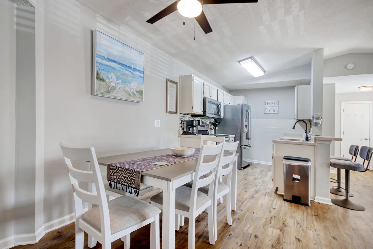 A view of a dining table set adjacent to visible kitchen appliances, with artwork on the wall adding personality to the space. This open layout shows the sightline between dining and kitchen, underlining connectivity for social cooking and family gatherings.