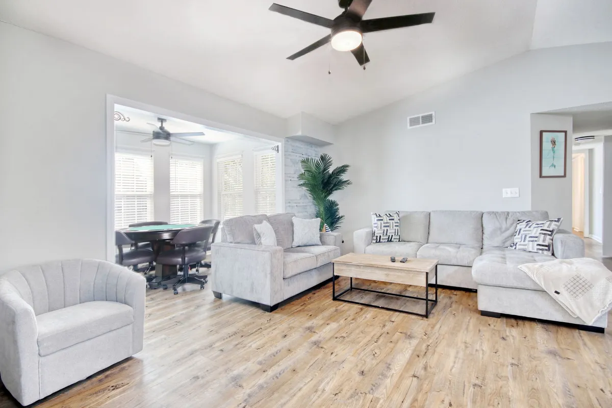 This scene features a comfortable living room with a plush sofa set, a coffee table, and an accent chair, complemented by a potted plant. The arrangement exudes warmth and is ideal for relaxing, socializing, or family gatherings. Large windows are implied by the abundance of natural light, further enhancing the welcoming atmosphere.