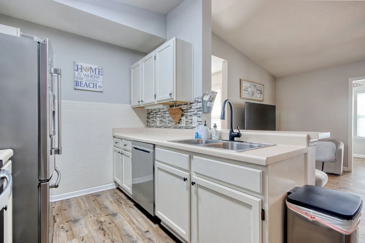 A welcoming kitchen scene with a focus on a modern sink, stainless steel appliances, a mosaic backsplash, and a decorative sign. The cozy setup suggests a space suitable for both quick breakfasts and family meal preparation, with everything a home chef might need.